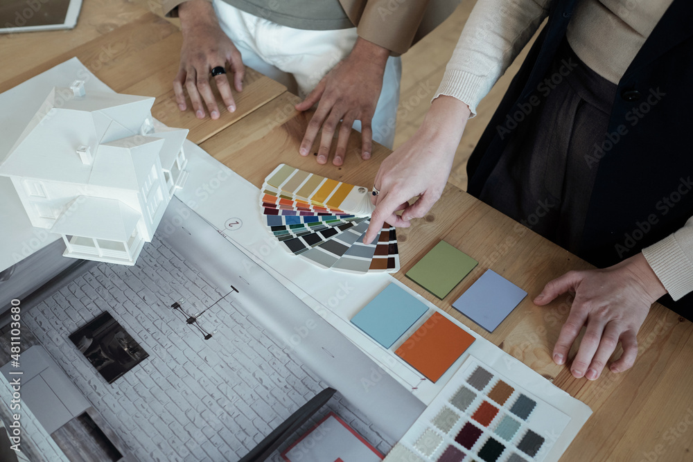 Poster hand of businesswoman pointing at color palette while consulting with male colleague over table with