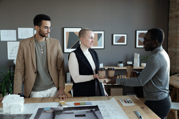 Happy young African man passing drinks to his intercultural colleagues during coffee break in office environment