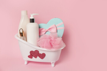 Obraz na płótnie Canvas White bathtub with body care products shampoo, lotion, cosmetic oil, washcloth on pink background. Love concept. Valentine's Day