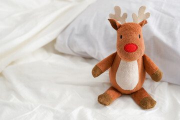 baby Toy deer sitting on white bed, copy space