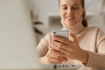 Closeup portrait of woman wearing beige casual style sweater holding cell phone in hands, using mobile phone for online communication with friends or writing post social networks.