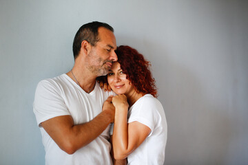 Naklejka premium Cute European middle-aged couple tender hugs against a gray wall. Man and woman together, support. gray plain background, copy space
