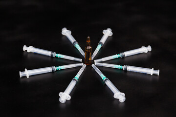 Syringes with needles spread out around the ampoule with medicine on a black background.