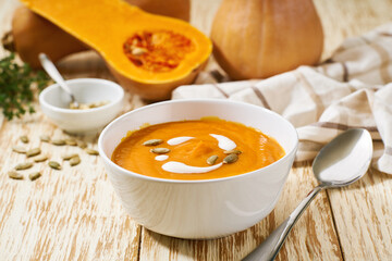 Bowl with butternut squash soup and pumpkin seeds  on a white wooden table, selective focus.