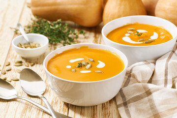 Delicious pumpkin soup in bowls with cream sauce on a white wooden table, selective focus.