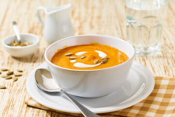 Bowl of homemade soup with organic pumpkin with cream sauce, on a white wooden table.