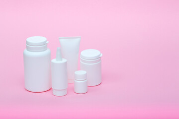 White different medecine or cosmetic jars on a pink background as a concept of cosmetology of medecine and treatment