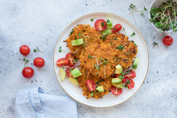 Crispy sweet potato fritters served with tomatoes, avocado and microgreens on white plate. Alternative plant based food. top view with copy space