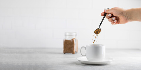 A woman adds instant coffee to a white mug on grey stone table. Copy space.