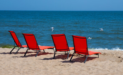 Red sunbeds on the beach. Nobody on the deck chairs. red deck chair on a shallow sandy beach, beach equipment
