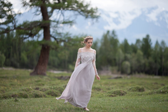 a girl in a royal image, a girl walks against the backdrop of mountains, a girl in a gray dress