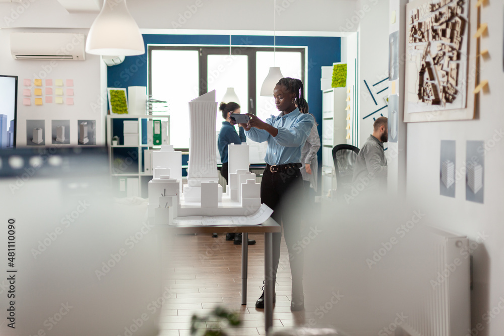 Poster architect working with smartphone to photograph maquette of skyscraper building complex. engineer wi