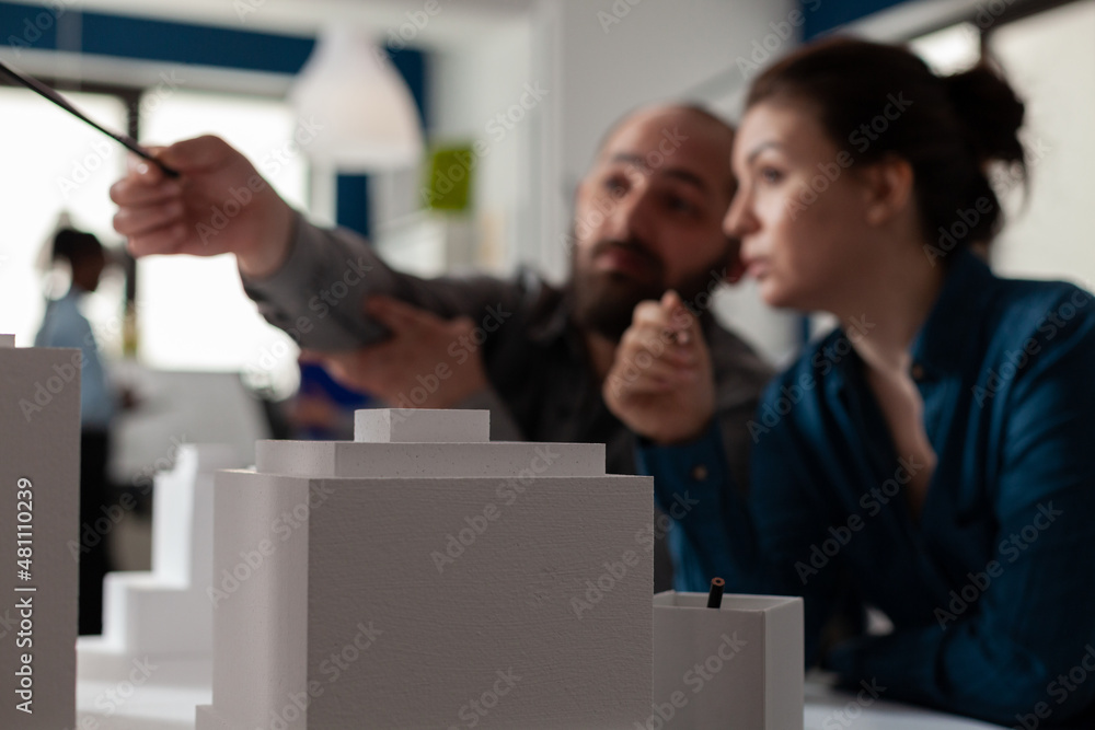 Poster closeup of white foam architectural scale model of buildings in front of architects team pointing at
