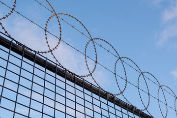 Looking up at circular barbed wire fence against blue sky diagonal juxtaposition