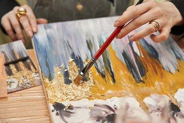 female hands apply gold potal to the picture, distributing it with a brush © Elena