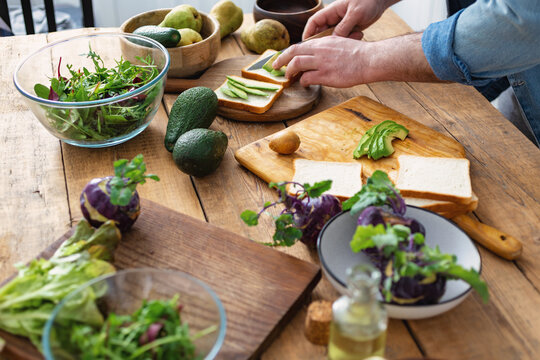 Cooking a healthy and tasty breakfast or lunch. Man preparing avocado sandwiches at home kitchen