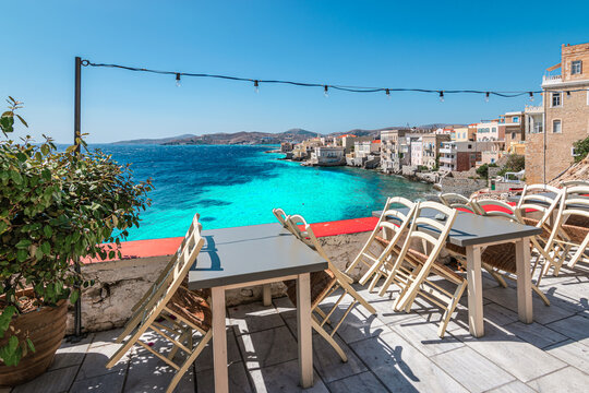 Empty chairs and tables of closed outdoor restaurant with sea view in Greece.