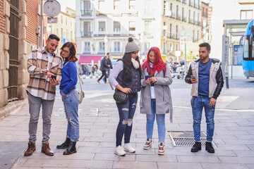 Hispanic man with smartphone looking at friends in outerwear browsing social media while standing on pavement on city street together