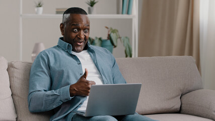 Excited mature man sitting looking at laptop screen reading email with good news rejoices in success celebrating victory actively dancing dance of winner wins online lottery shows gesture of approval