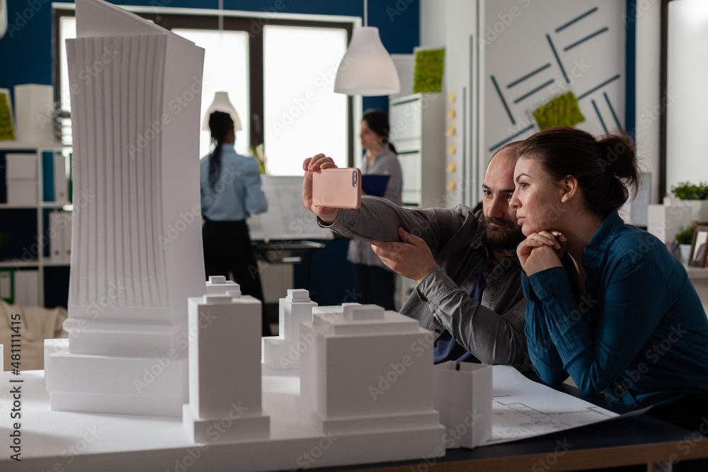 Poster team of two architect colleagues using smartphone in videocall conference with client presenting des