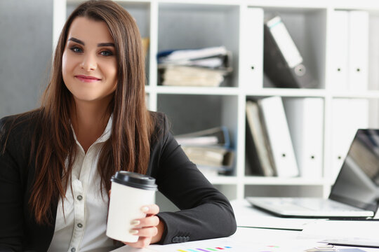 Attractive worker in suit holding cup of coffee, posing on working place in office