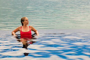 Young woman relax in infinity pool with lake view. Natural hot spring spa under Batur volcano....