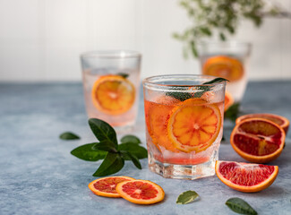 Gin and tonic alcohol drink with blood Sicilian oranges and ice on blue concrete background. Cold refreshing cocktail.