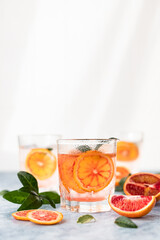 Gin and tonic alcohol drink with blood Sicilian oranges and ice on blue concrete background. Cold...