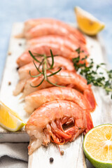 Raw Argentine shrimps on white wooden cutting board with lime, herbs and pepper. Seafood.