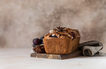 Homemade spicy plum cake decorated with almond on a wooden board, concrete background. Loaf cake with plum, spices and almond.