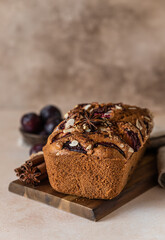 Homemade spicy plum cake decorated with almond on a wooden board, concrete background. Loaf cake with plum, spices and almond.