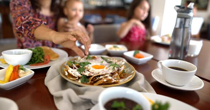 Hand picking tortilla chip with cheese and coriander from plate of chilaquiles