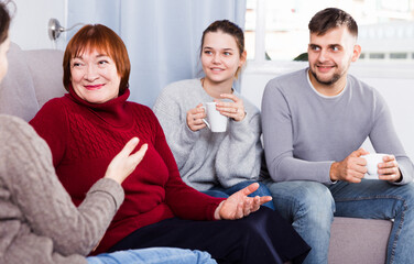 Smiling mature lady with adult children enjoying conversation with female friend at home