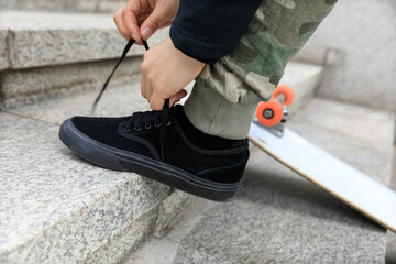 Skateboarder tying shoelace while skateboard outdoors in city