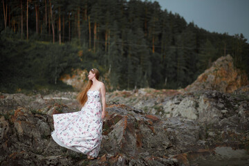 blonde with long hair, a girl walks by a mountain river before the rain, a gloomy heavy sky, clouds, the Katun River, the Altai Mountains, an art photo session, a dress with a floral print