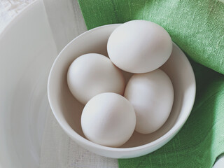 Top view of fresh white chicken eggs in a white plate on a green background. Natural linen. Ingredients. Easter. Shrovetide. Russian cuisine, traditions
