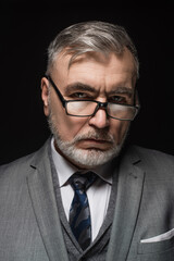 serious senior businessman in eyeglasses looking at camera isolated on black.