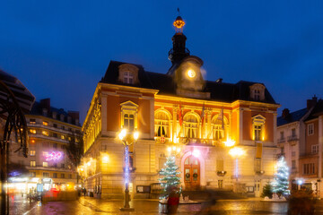 Fototapeta na wymiar Night view of Chambery city hall surrounded by fir trees and street lamps decorated with traditional Christmas lights in central square in winter, France