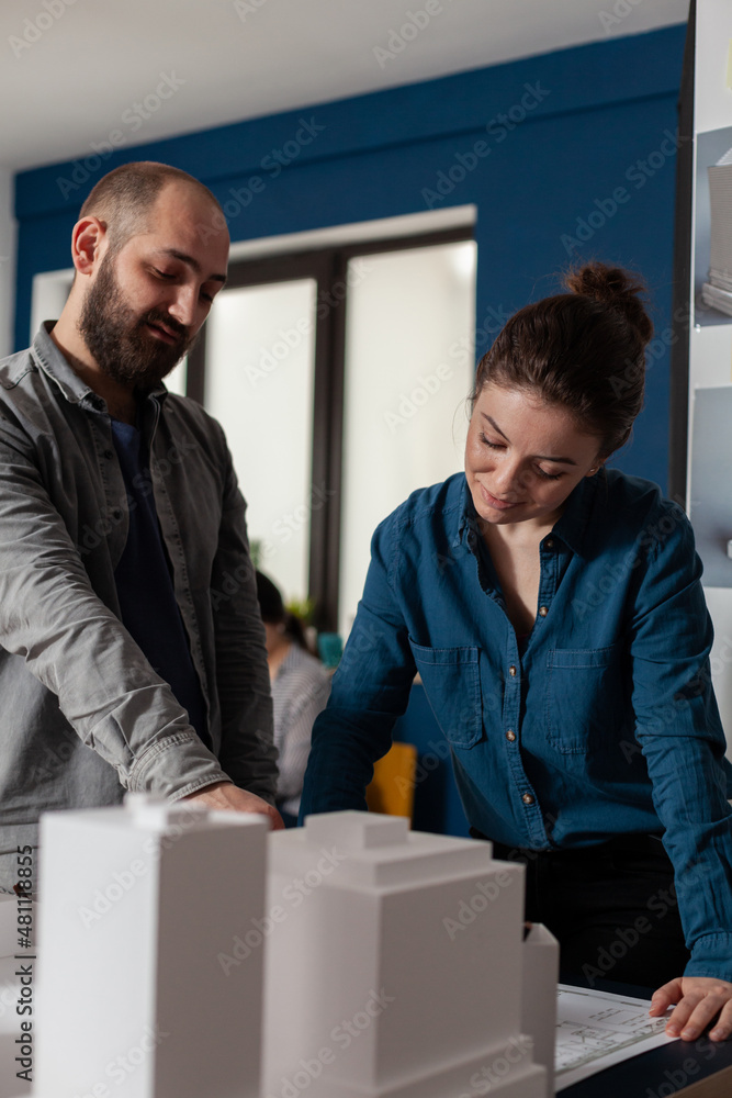 Poster architect pointing at architectural blueprints collaborating with colleague engineer in modern offic