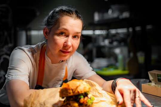 young woman chef with burger sitting in the kitchen of a cafe or restaurant