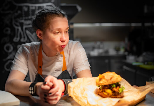 young woman chef with burger sitting in the kitchen of a cafe or restaurant