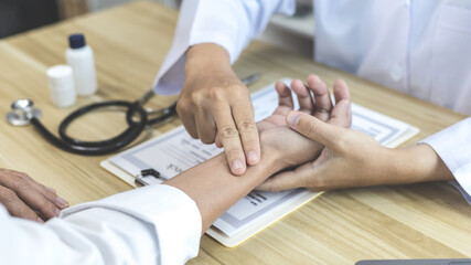 Medical professional measures the pulse of a male patient's wrist to check his heart rate in the hospital's examination room, Doctor checking patient health, Initial symptom check.