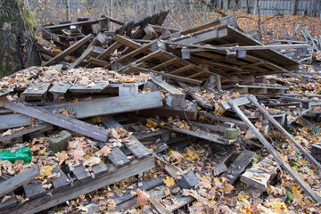 scattered pile of old dirty wooden pallets, wood planks and hardwood timber boards on autumn dry and yellow leaves ground