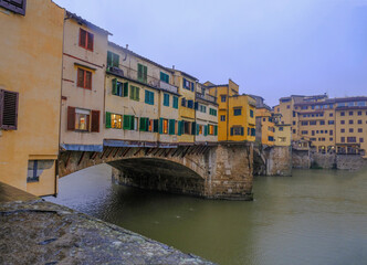 Fototapeta na wymiar Florence, Italy: View on the Florence Ponte Vecchio with colorful stores on a rainy day across river Arno and dramatic gray sky 