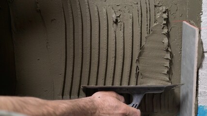 The process of laying ceramic floor tiles. The builder applies an adhesive base to ceramic tiles....