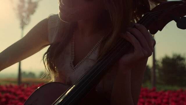 Closeup inspired young woman playing cello in blooming summer garden outdoors.