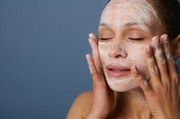 Beautiful woman massaging her face while removing make-up using a foam cleansing cosmetic product,...