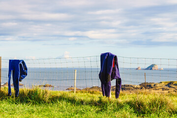 Diving suis drying on fence with sea view