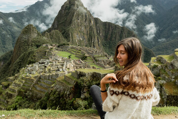 A beautiful young tourist sitting on a the edge of the hill with a stunning view on Machu Picchu