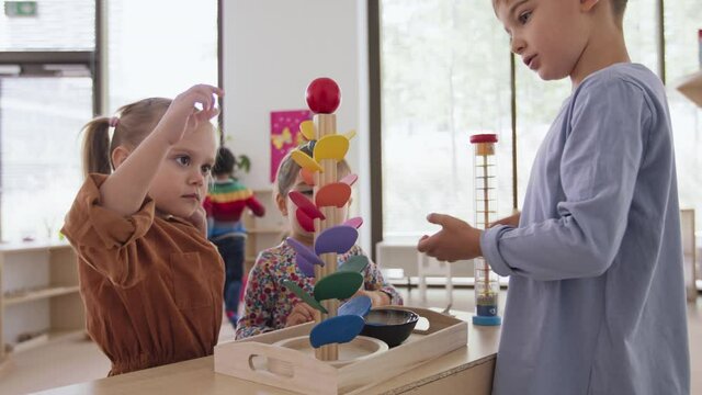 Children playing with marble run indoors in nursery, montessori education.